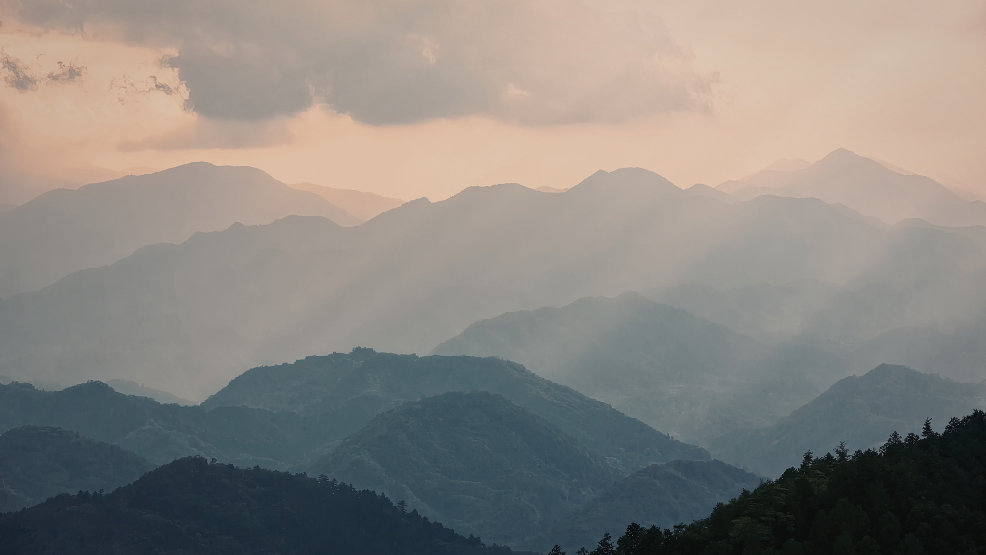 Layered mountain range under a cloudy sky during sunset or sunrise.