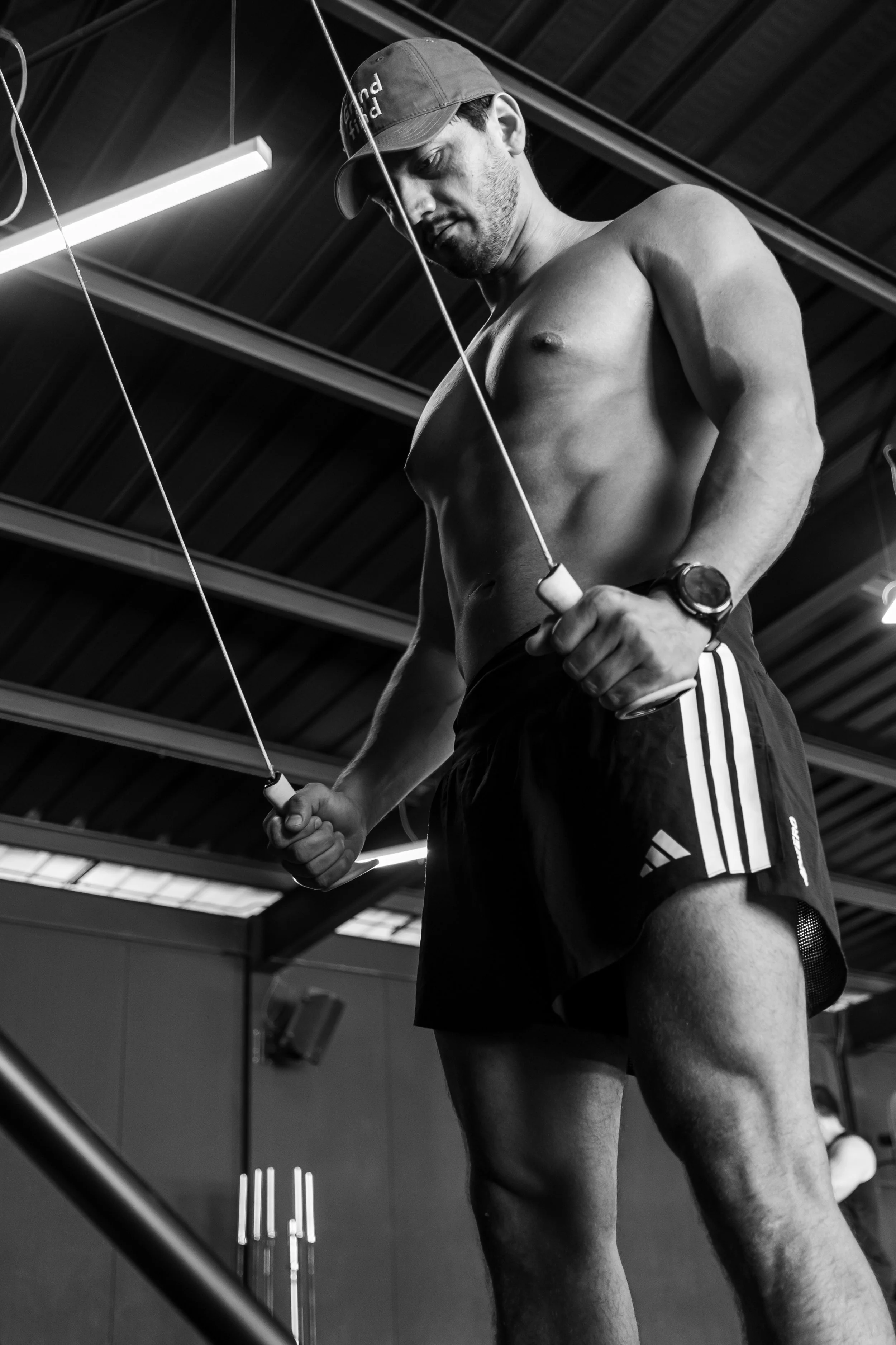 Hombre sin camiseta con pantalones cortos haciendo ejercicio en un gimnasio con estructura de metal y iluminación artificial.