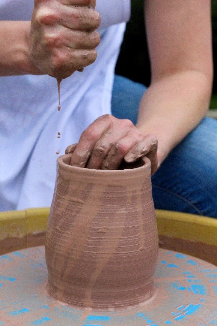 Person shaping wet clay on a pottery wheel, with hands inside a ceramic pot.