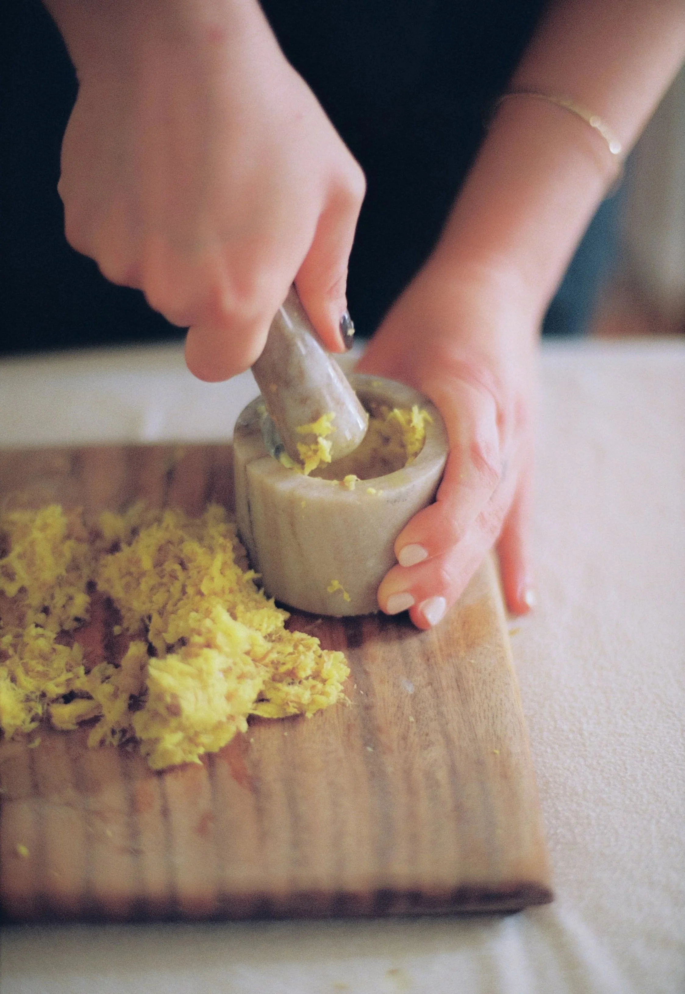 Person using a mortar and pestle to grind yellow ingredients on a wooden cutting board.
