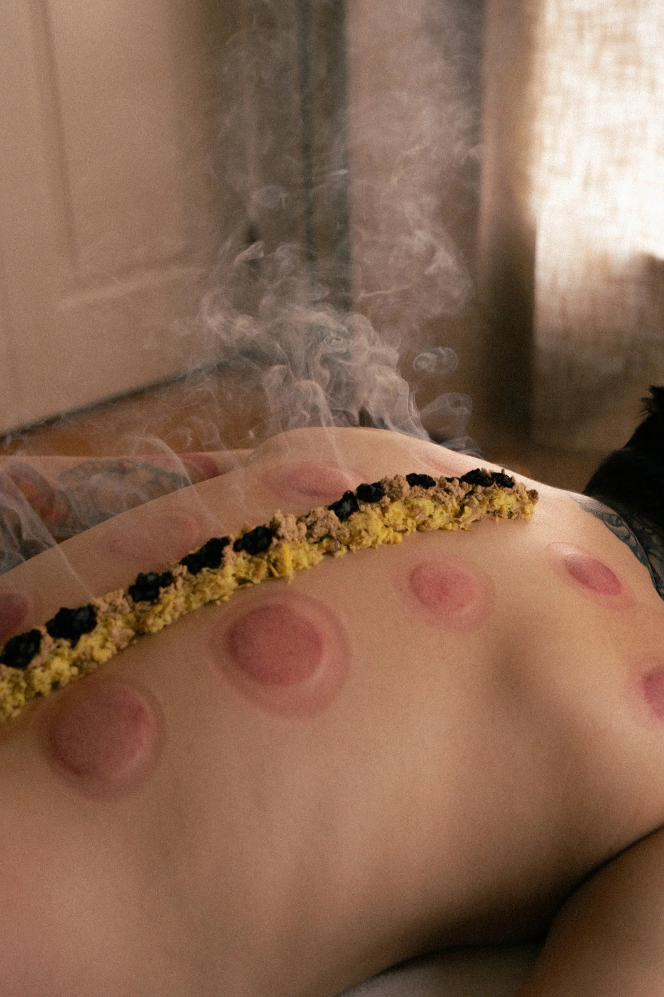 Close-up of a person's lower back with a strip of medical tape, dotted with black and yellow dots, possibly a chiropractic or medical treatment, with wisps of steam or smoke rising from the area.