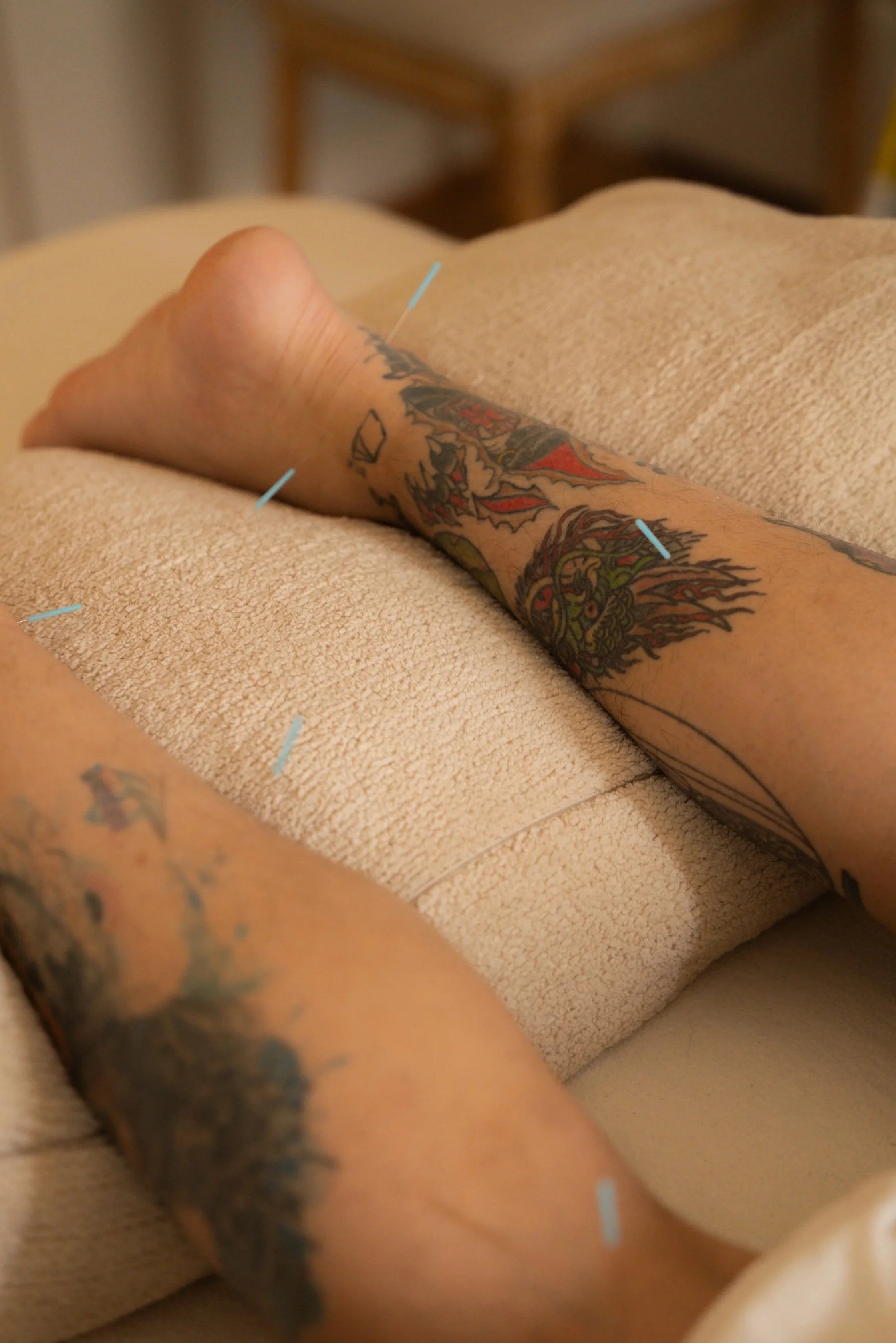 Close-up of a person's tattooed arm resting on a beige textured surface, with a blurred background.
