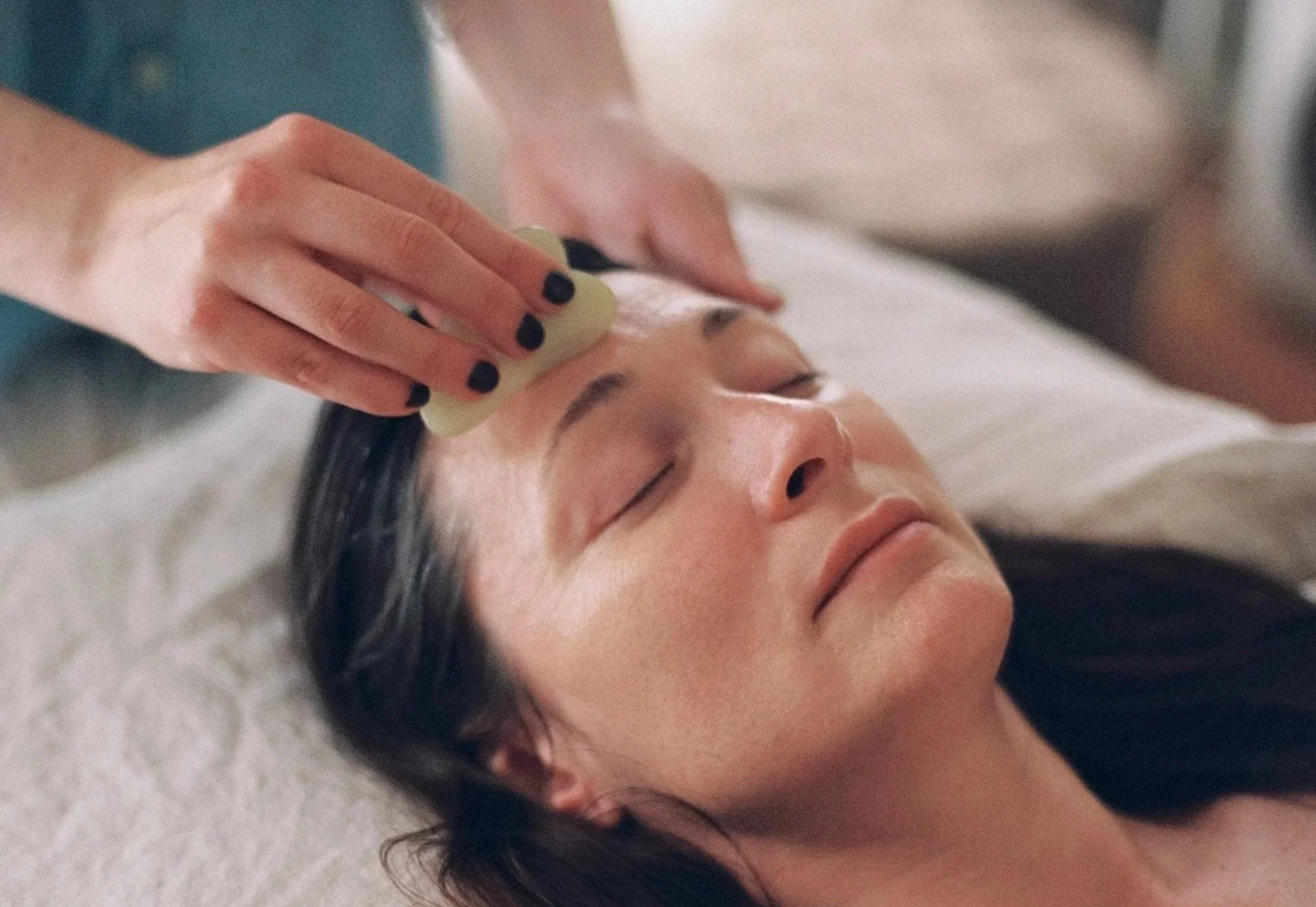 A person receiving a facial treatment with a sponge or cloth on their forehead while lying down with eyes closed.