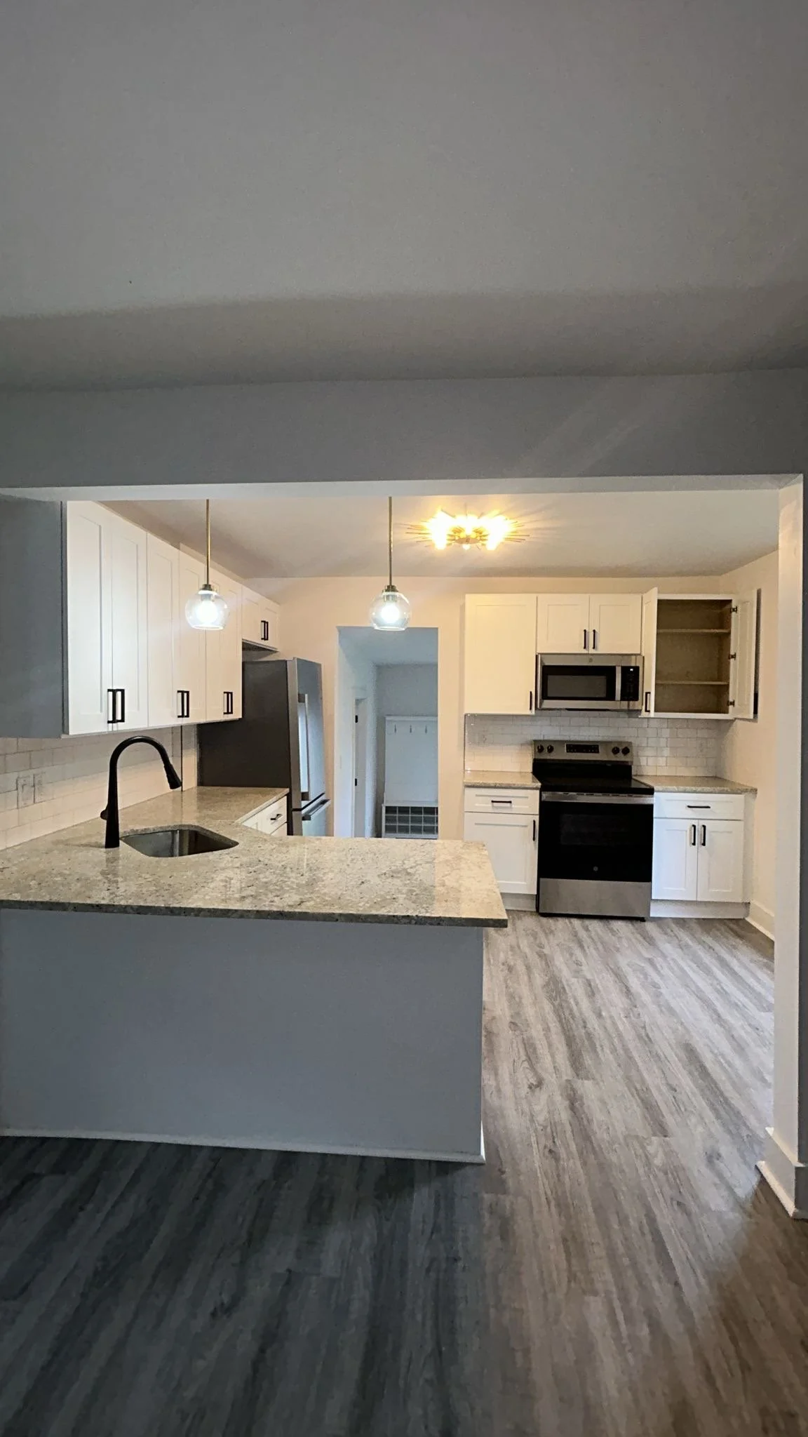 Modern kitchen with white cabinets, stainless steel appliances, granite countertops, pendant lights over an island, and wood-look flooring.