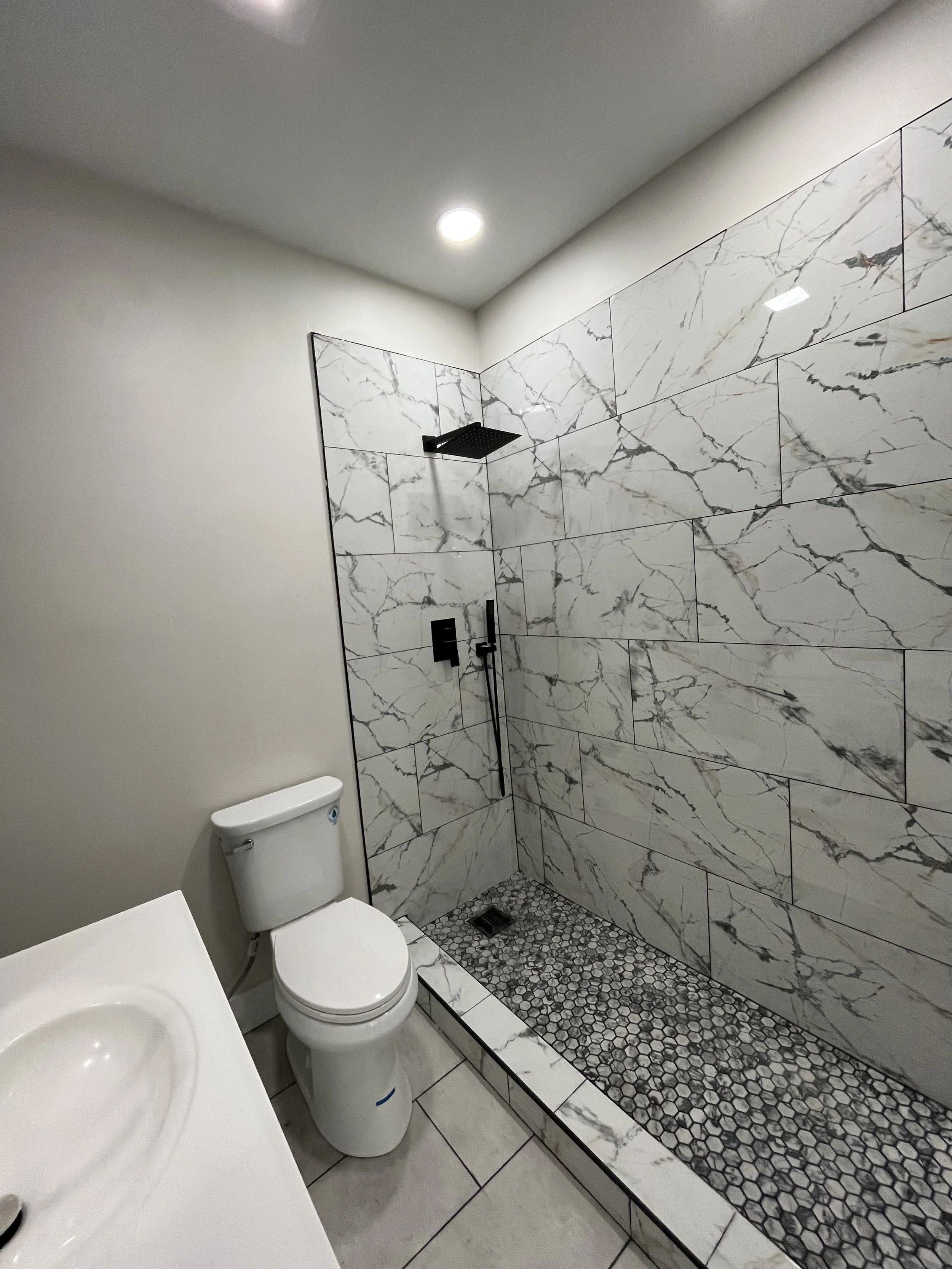 Modern bathroom with marble tiled shower, black fixtures, and a white toilet