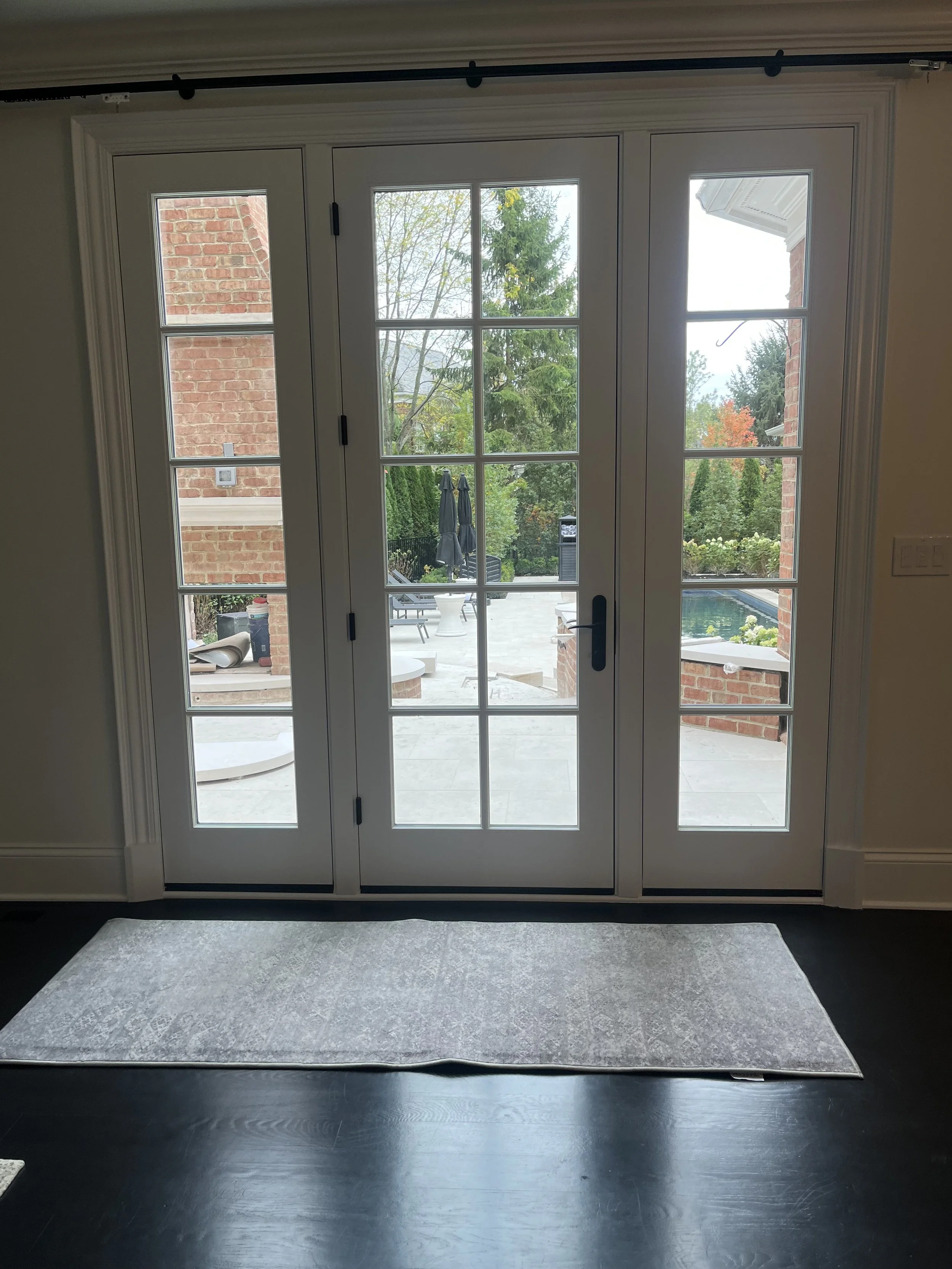 Interior view of double glass doors leading to outdoor patio and garden with trees and patio furniture.