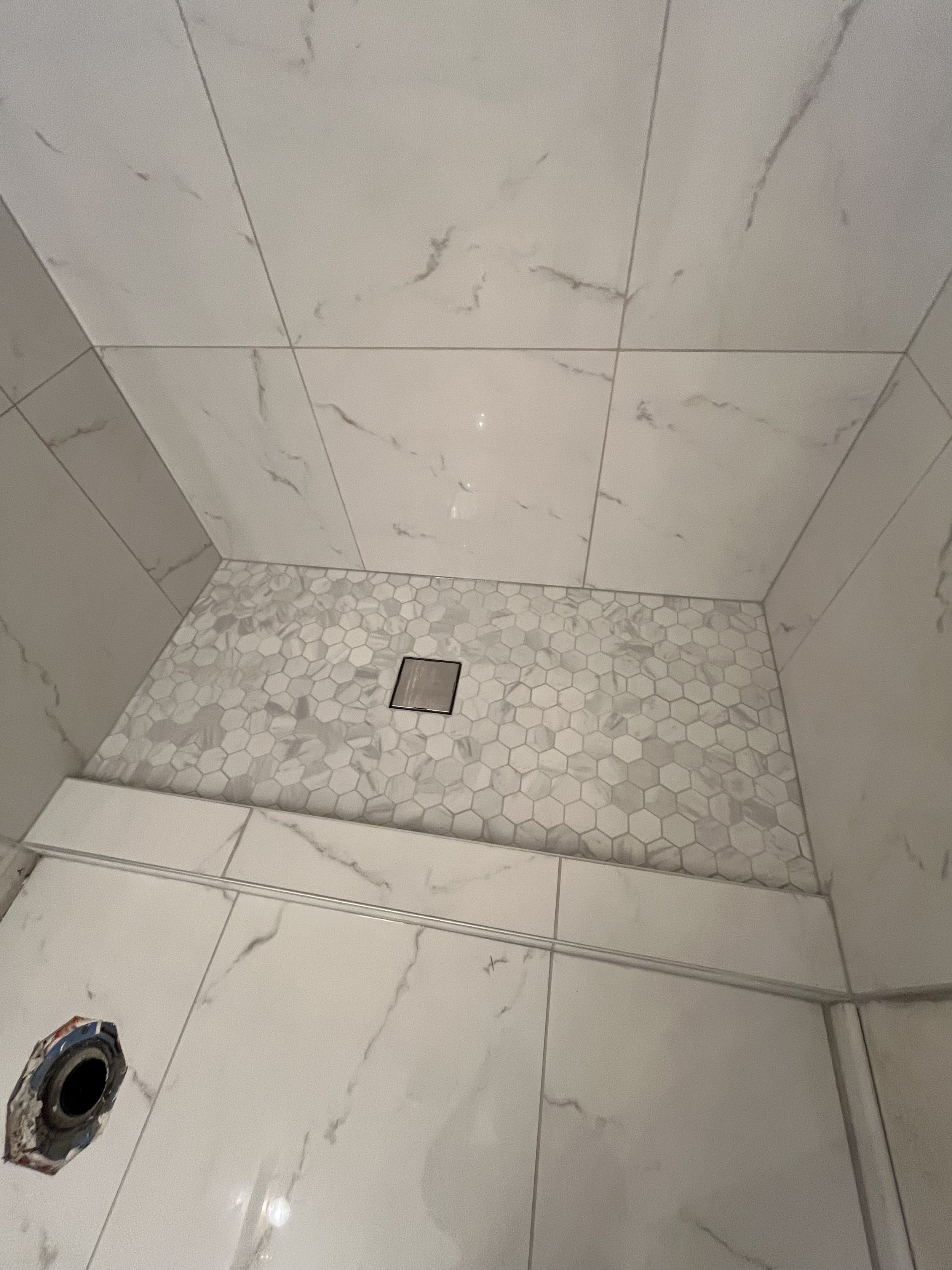Interior of a shower with large marble tiles on the walls, small hexagon tiles on the shower floor, and a drain in the center.