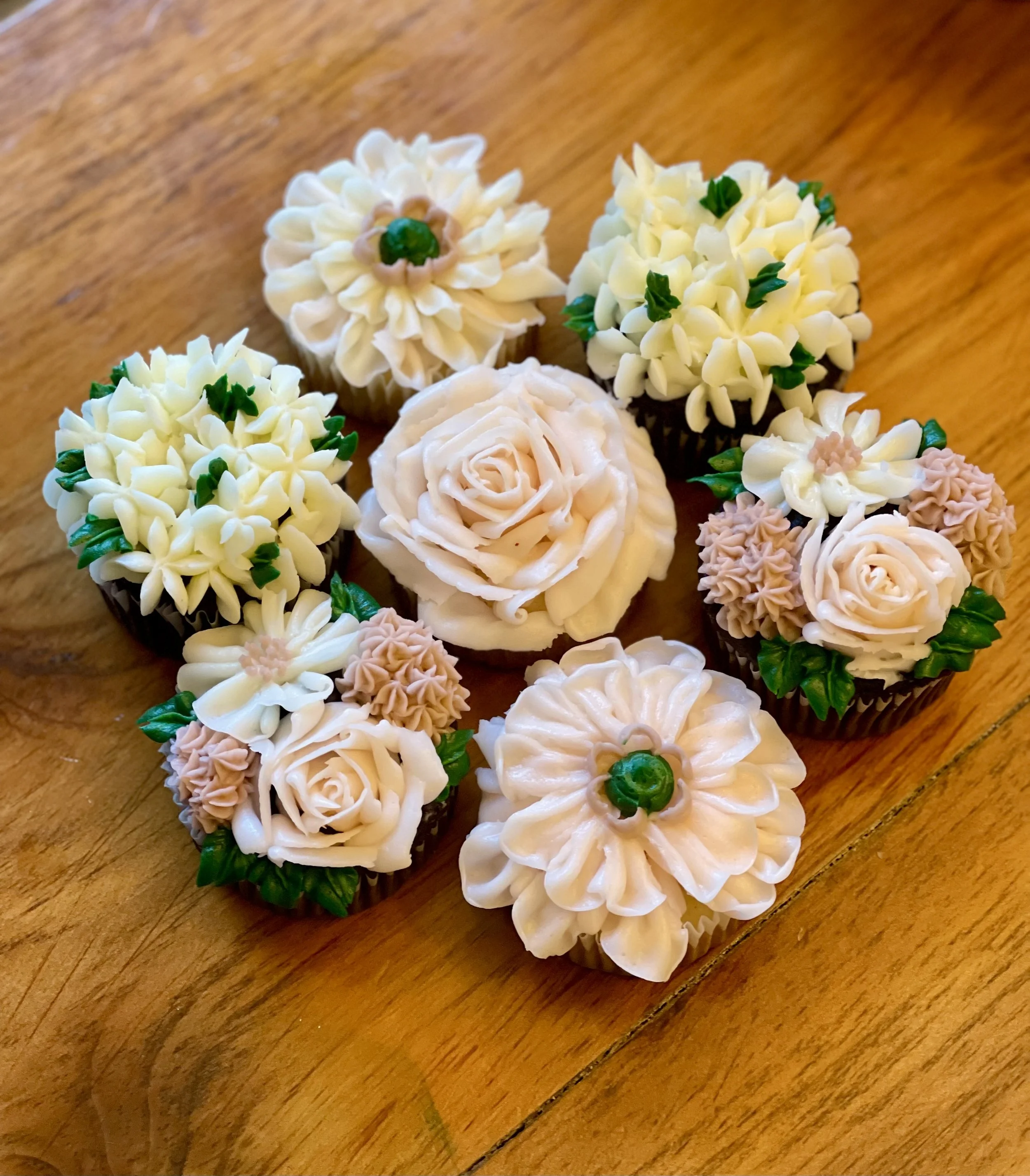 Decorative cupcakes with floral and rose frosting designs on a wooden surface.