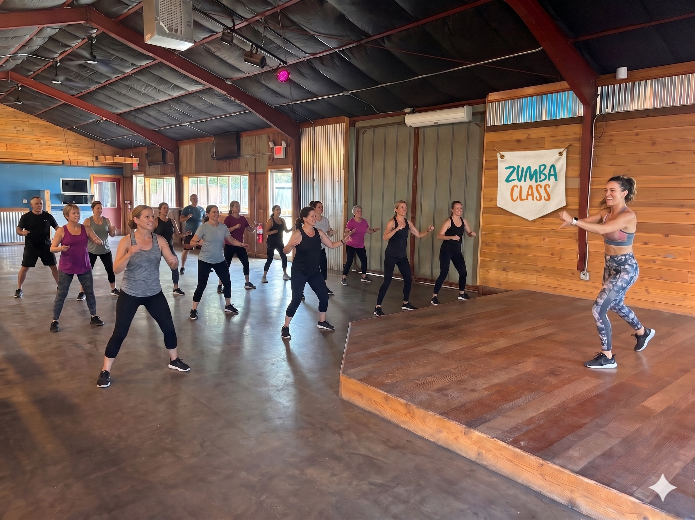 A group of people participating in a Zumba class led by an instructor on a small stage, inside a wooden-finished fitness studio with high ceiling and large windows.