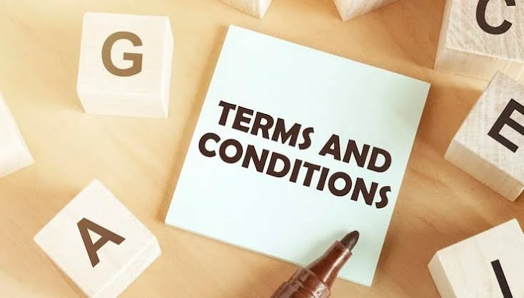A light blue paper with the words 'Terms and Conditions' written in bold black letters, surrounded by wooden blocks with letters G, A, and E on them, and a brown marker pen pointing at the paper.