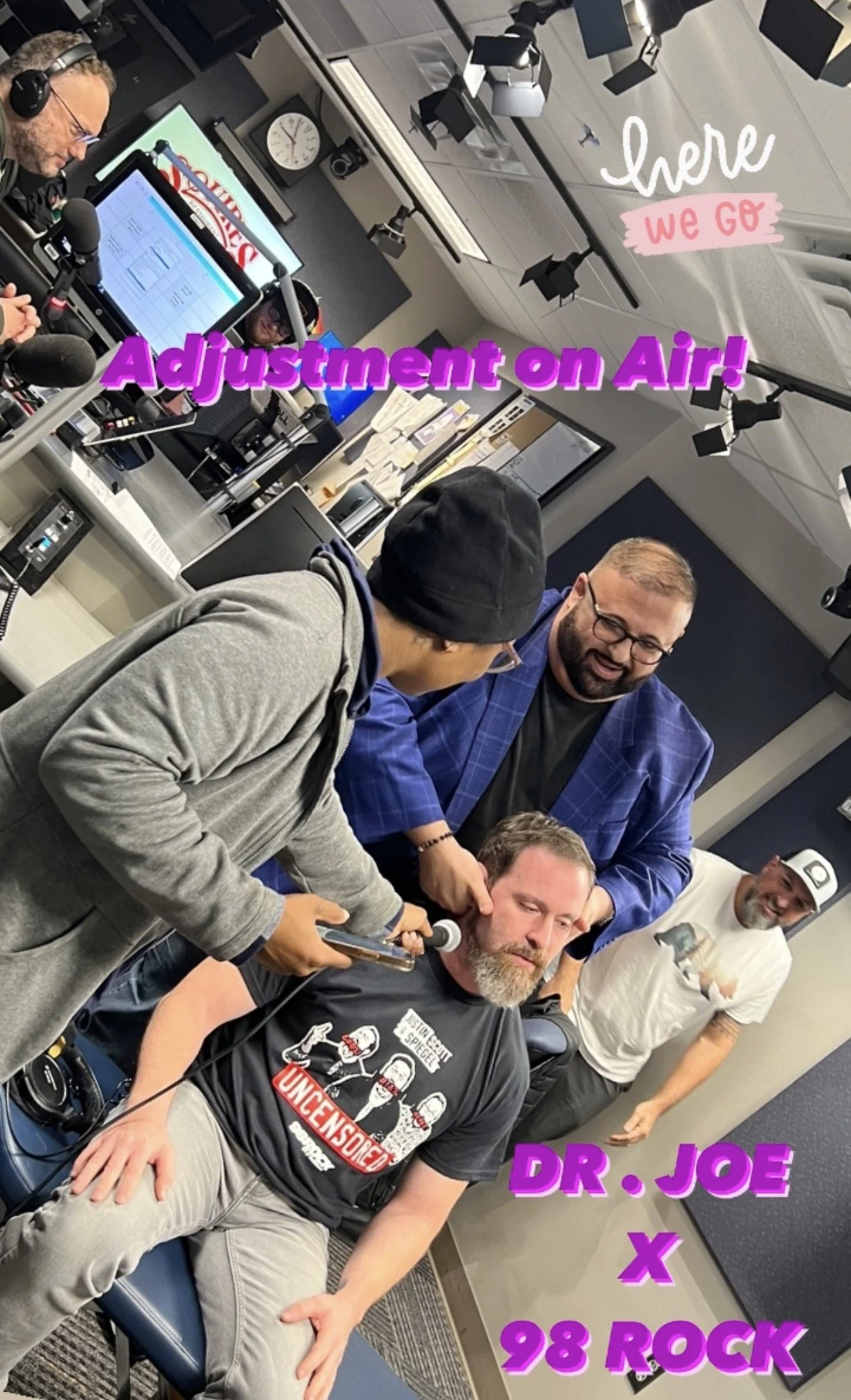 A radio station studio with a person wearing headphones and working at a microphone, people gathered around a seated man with a beard, wearing a t-shirt, holding a microphone near his mouth, others standing around smiling. The room has professional lighting, monitors, desks, and a clock on the wall. The image has overlaid text reading "here we go" and "Adjustment on air!" and details about the show "DR. JOE x 98 ROCK."