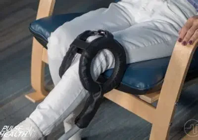 A person in white pants sitting on a wooden chair with a police belt and handcuffs draped over their lap.