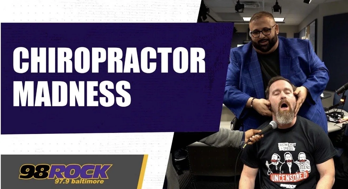 A man with his eyes closed and mouth open is receiving a chiropractic adjustment while a chiropractor presses on his neck. A large sign reads 'Chiropractor Madness' and there is a 98 Rock logo in the bottom corner.