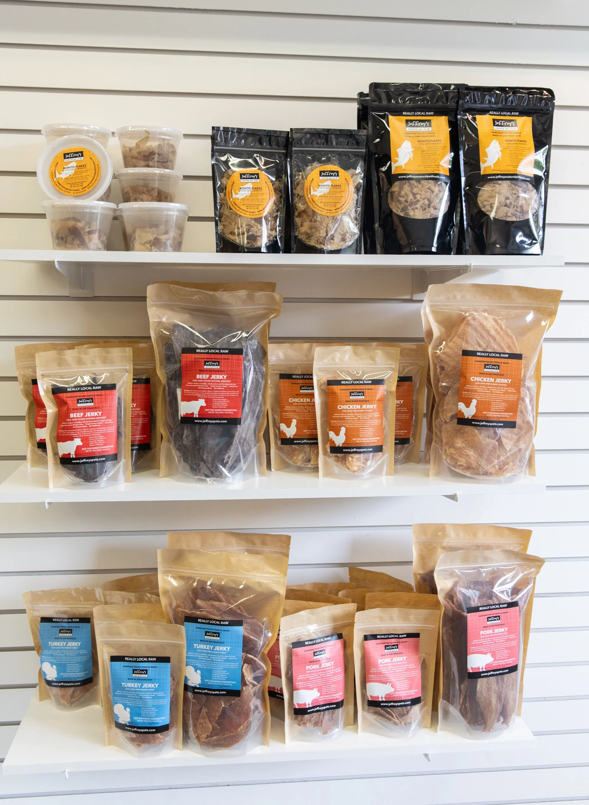 Shelf display of packaged pet treats, including beef, chicken, turkey, and pork jerky in various sizes.