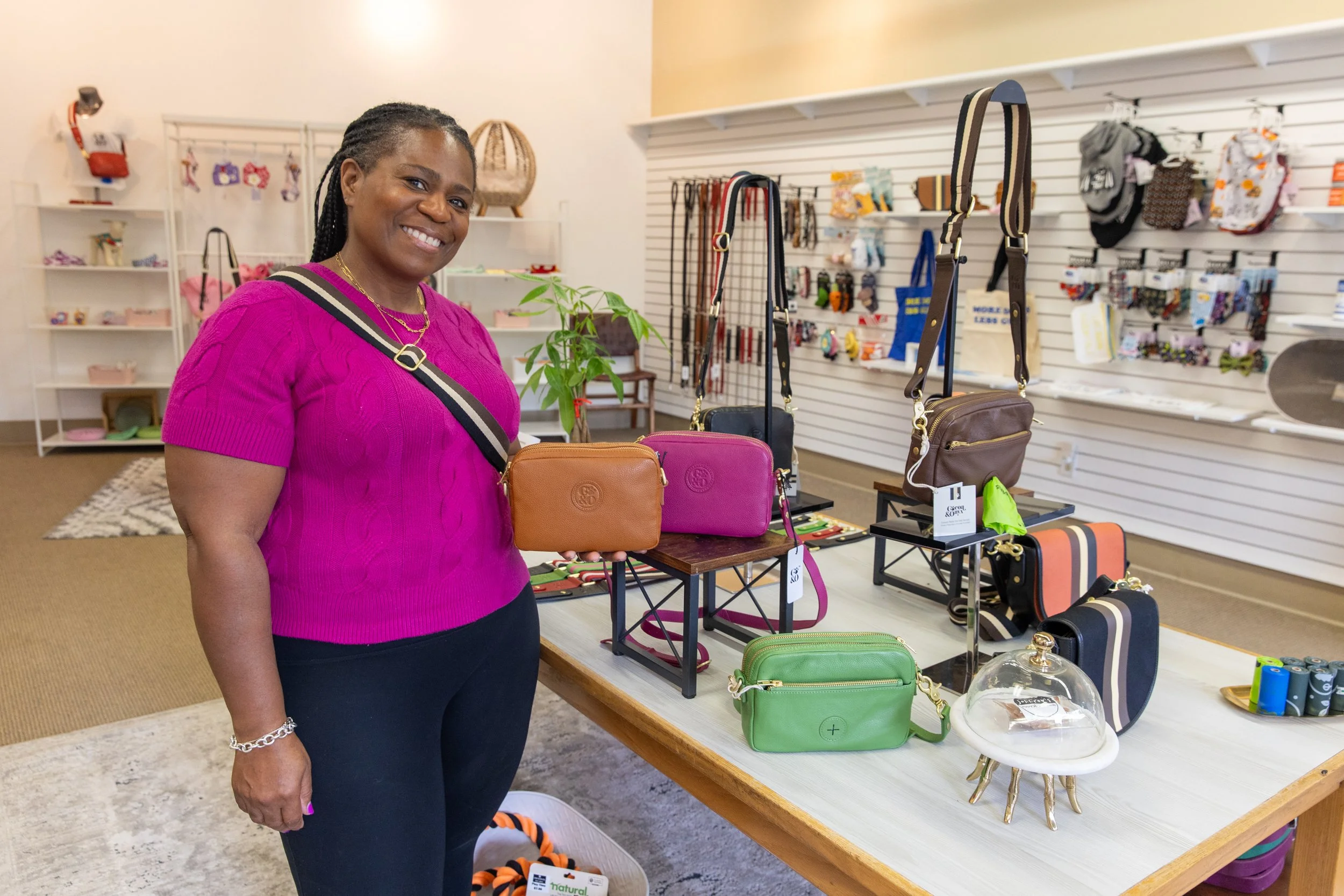 A woman wearing a pink top and black pants standing in a store with handbags and accessories on display.