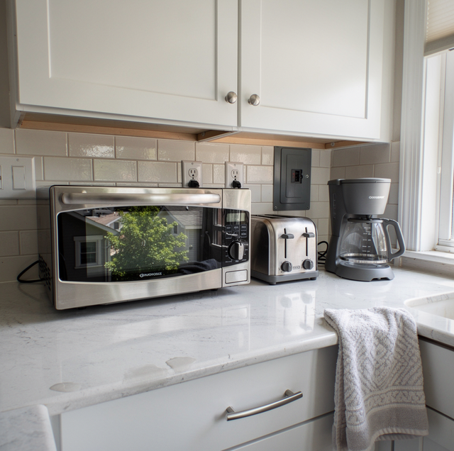 Kitchen counter with microwave, toaster, and coffee maker under white cabinets and subway tile backsplash.