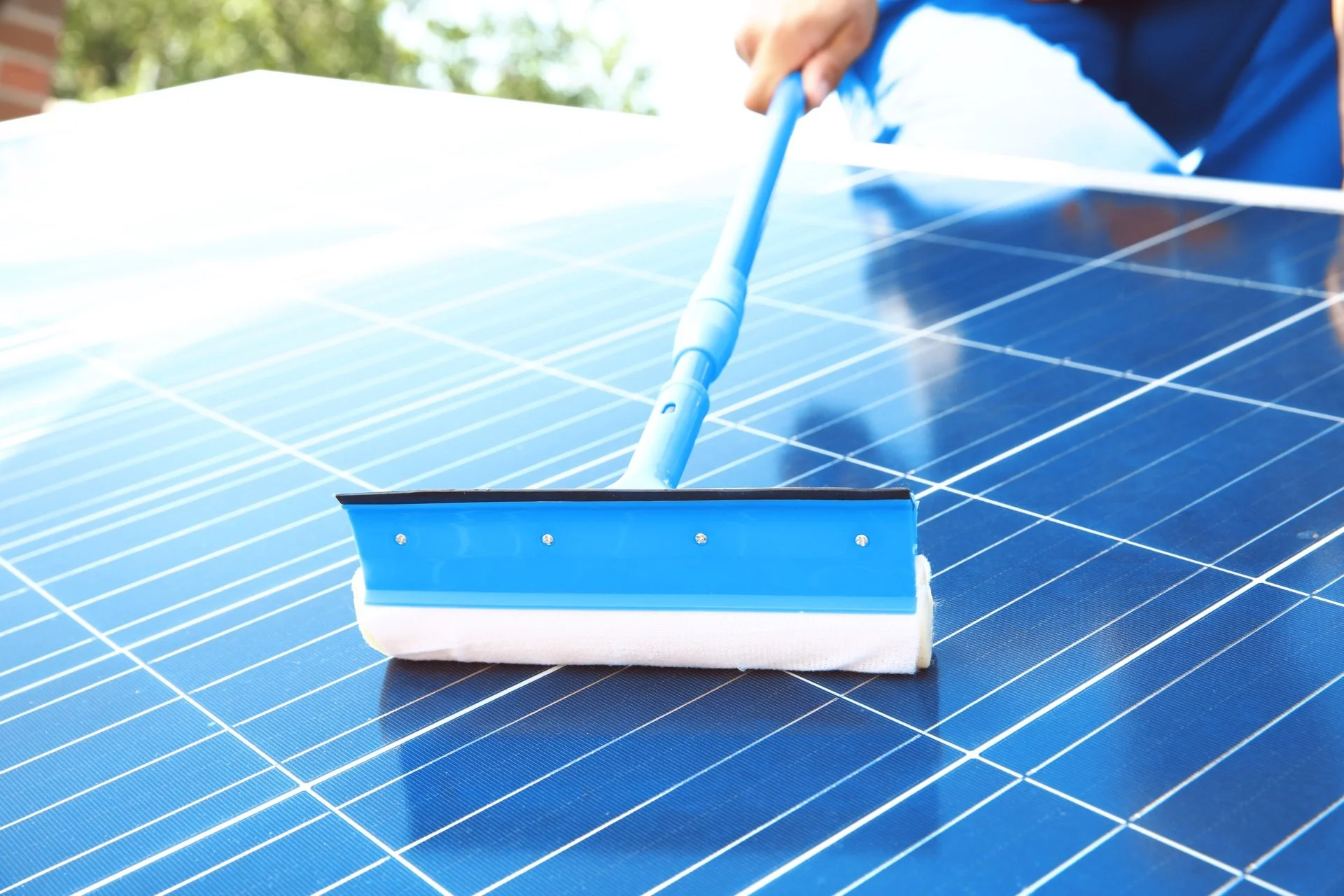Person cleaning solar panels with a blue squeegee on sunny day.