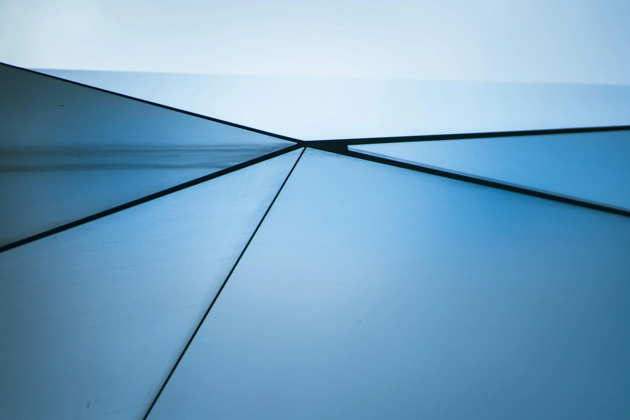 Close-up view of modern blue glass building reflecting the sky, showing geometric lines and shapes.