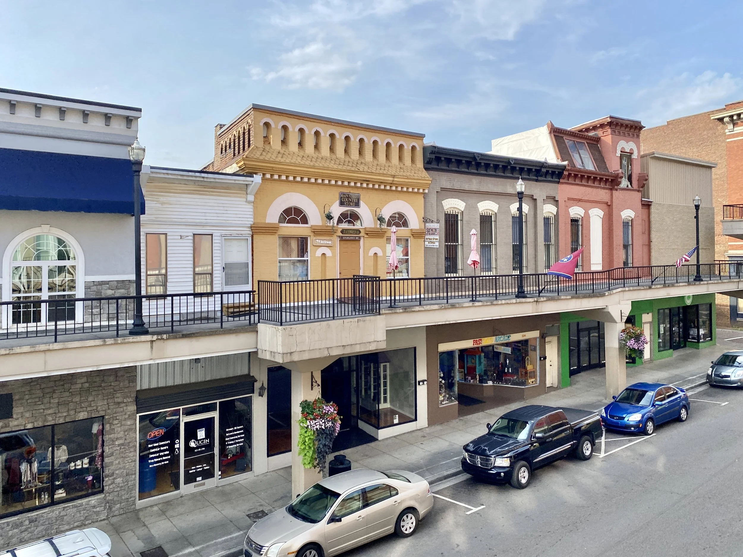 Street view of a small town with colorful storefronts and parked cars.