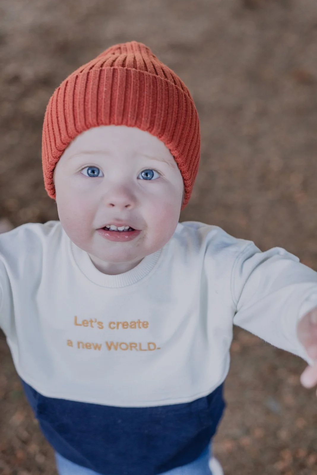 Ung gutt med blå øyne, rød lue og hvit t-skjorte som sier 'Let's create a new WORLD'.