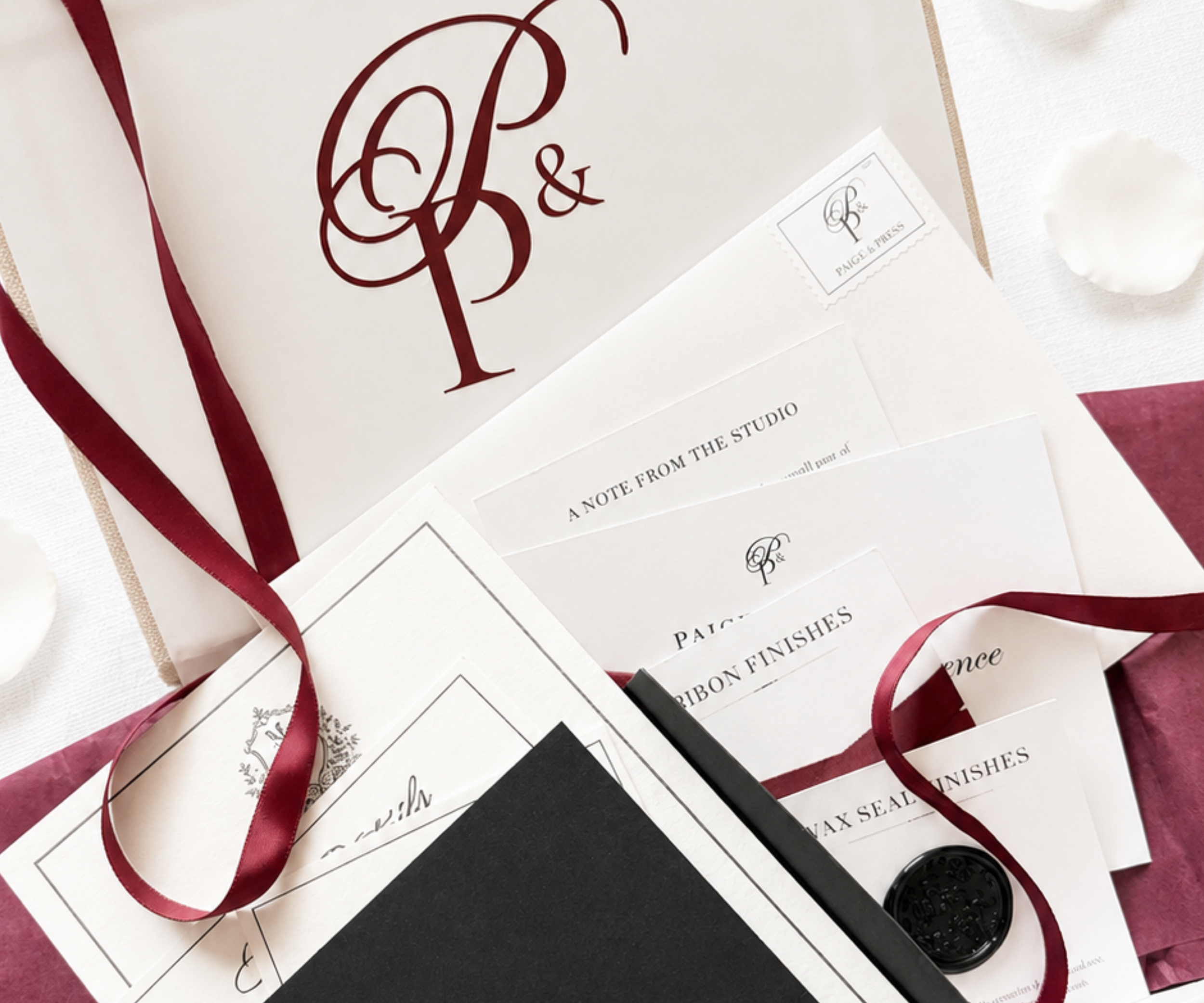 Paige & Press Sample Experience close-up of a luxury letterpress wedding invitation suite featuring a custom monogram, burgundy ribbon, black wax seal, and heirloom-inspired details.