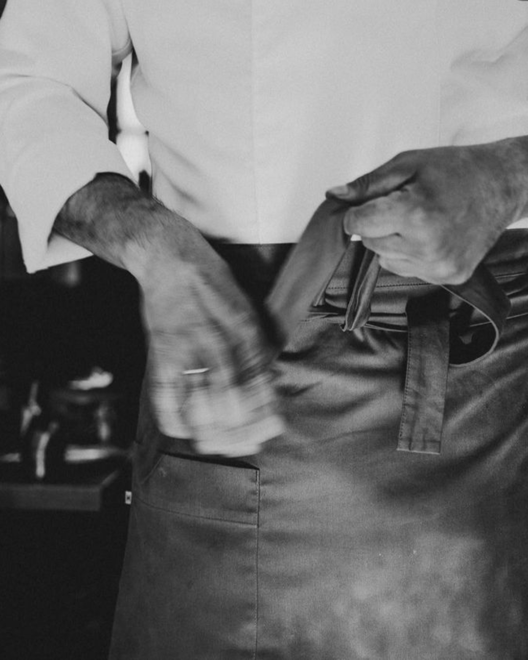 Close-up black and white photo of a person wearing a long-sleeve shirt, holding a wallet, and reaching into a pocket.