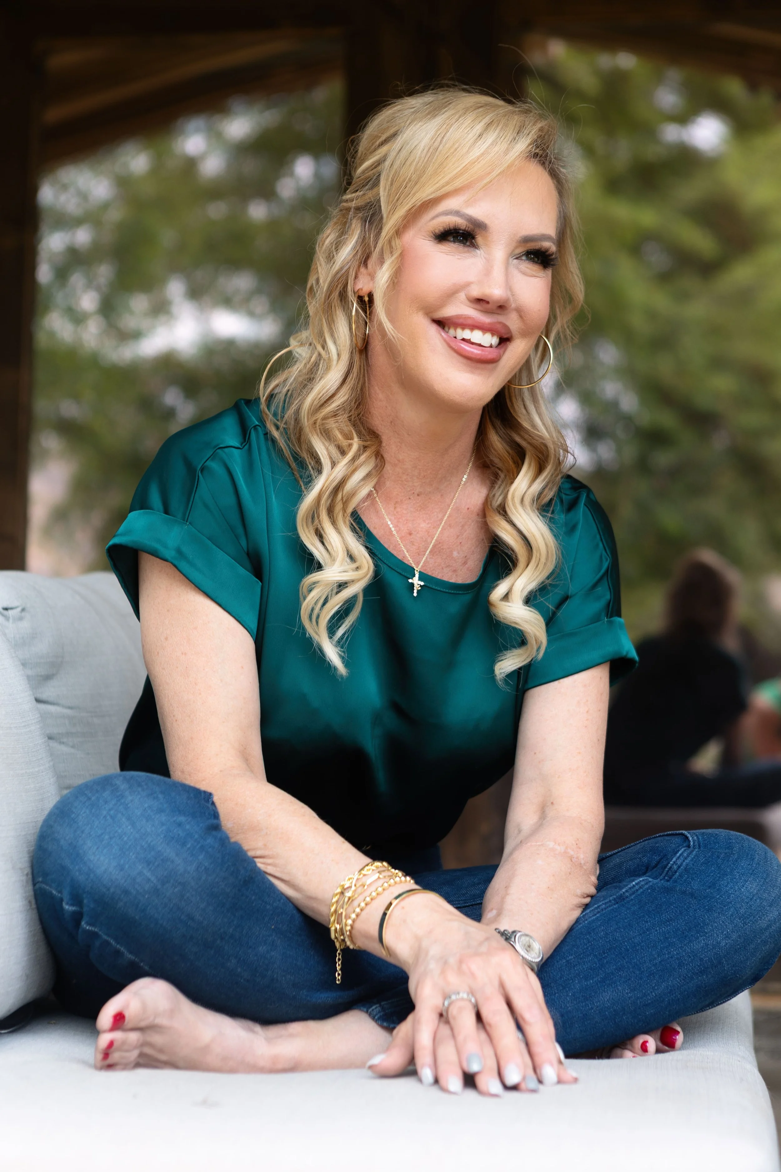 Sarah Engelhardt sitting cross-legged outdoors on a cushioned seat, smiling