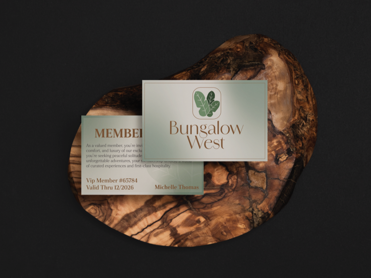 Business cards on a polished wooden surface, with one card reading "Bungalow West" and featuring a green leaf logo, set against a black background.