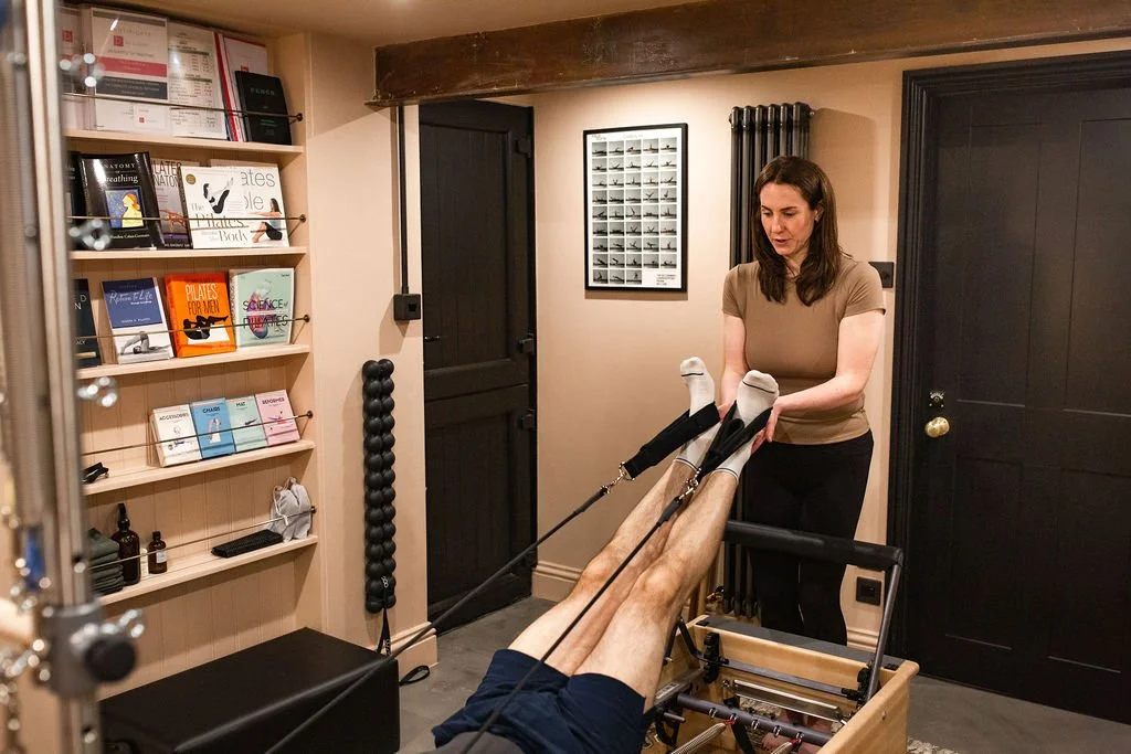Woman helping a client exercise legs with resistance bands in a home workout room decorated with books and framed pictures.