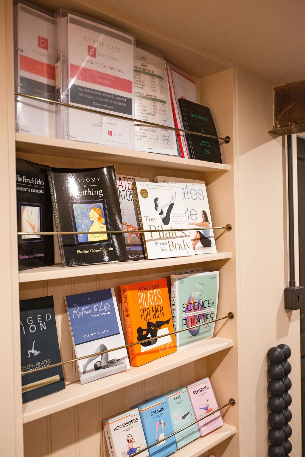 Books on fitness, anatomy, Pilates, and exercise on wooden shelves in a fitness studio.