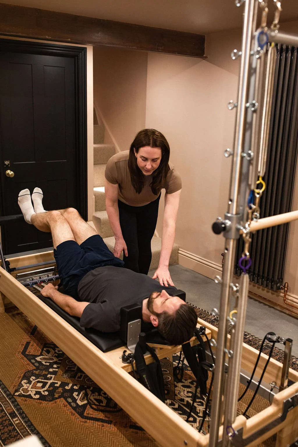 A man lying on a therapy bed with a harness, being assisted by a woman in a brown shirt, in a therapy or rehabilitation room.