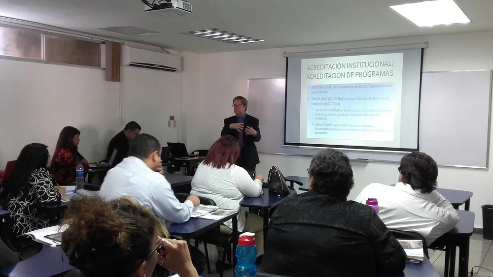 Clase o reunión académica con un presentador frente a una diapositiva que habla sobre acreditación institucional y de programas en un aula de clases con varias personas sentadas.