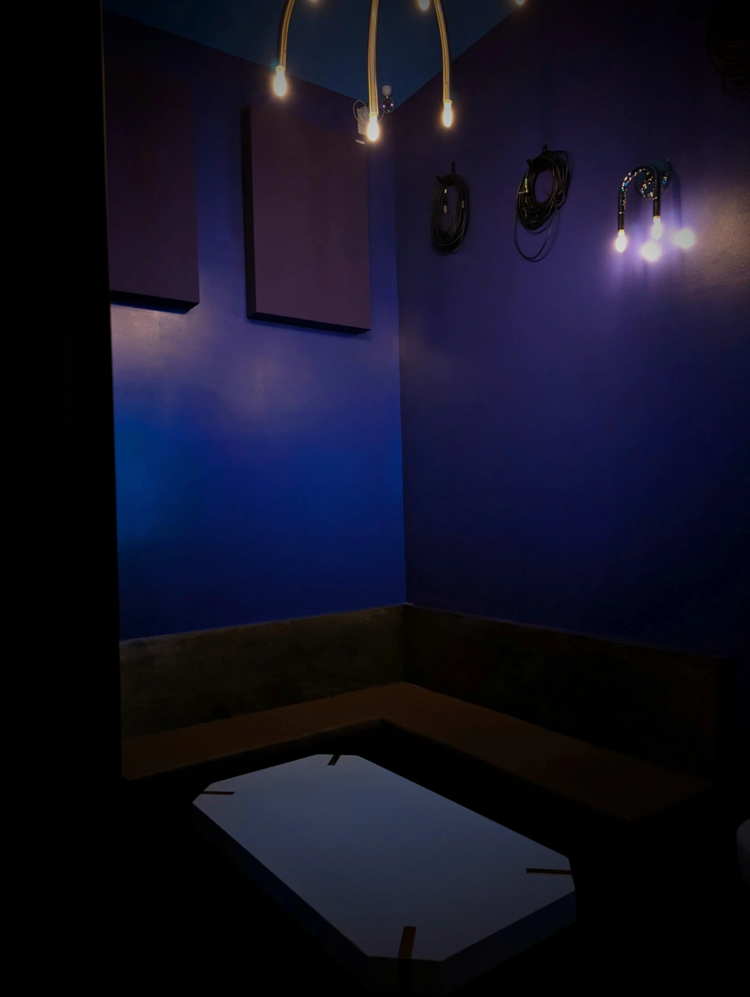A dark blue room with three hanging light bulbs and black cables on the wall. A black table or object is in the foreground.