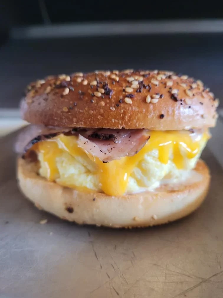 Close-up of a breakfast sandwich with eggs, cheese, ham, and a sesame seed bagel bun.