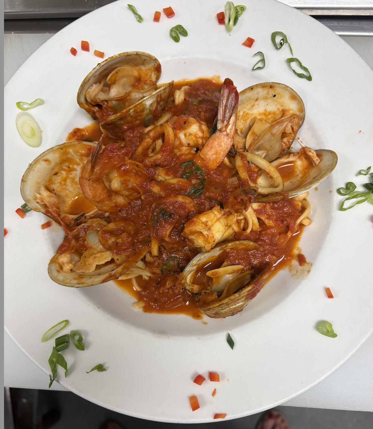Seafood pasta with shellfish, shrimp, and tomato sauce garnished with green onions on a white plate.