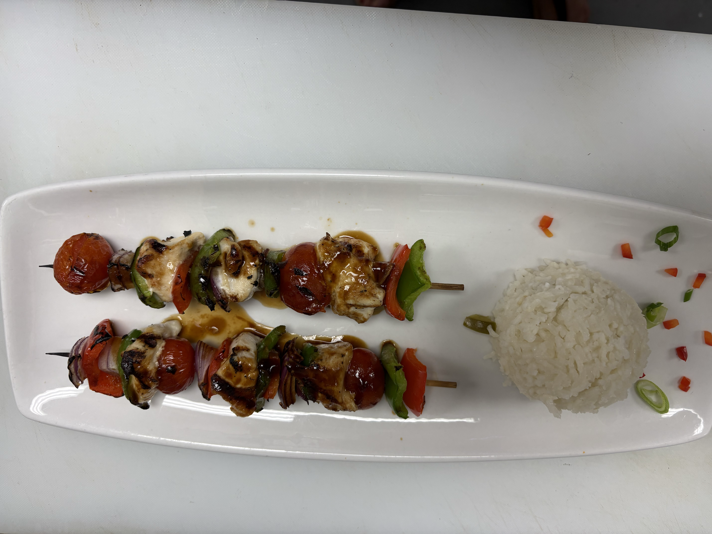 Skewered grilled chicken and vegetables with side of white rice on a white rectangular plate