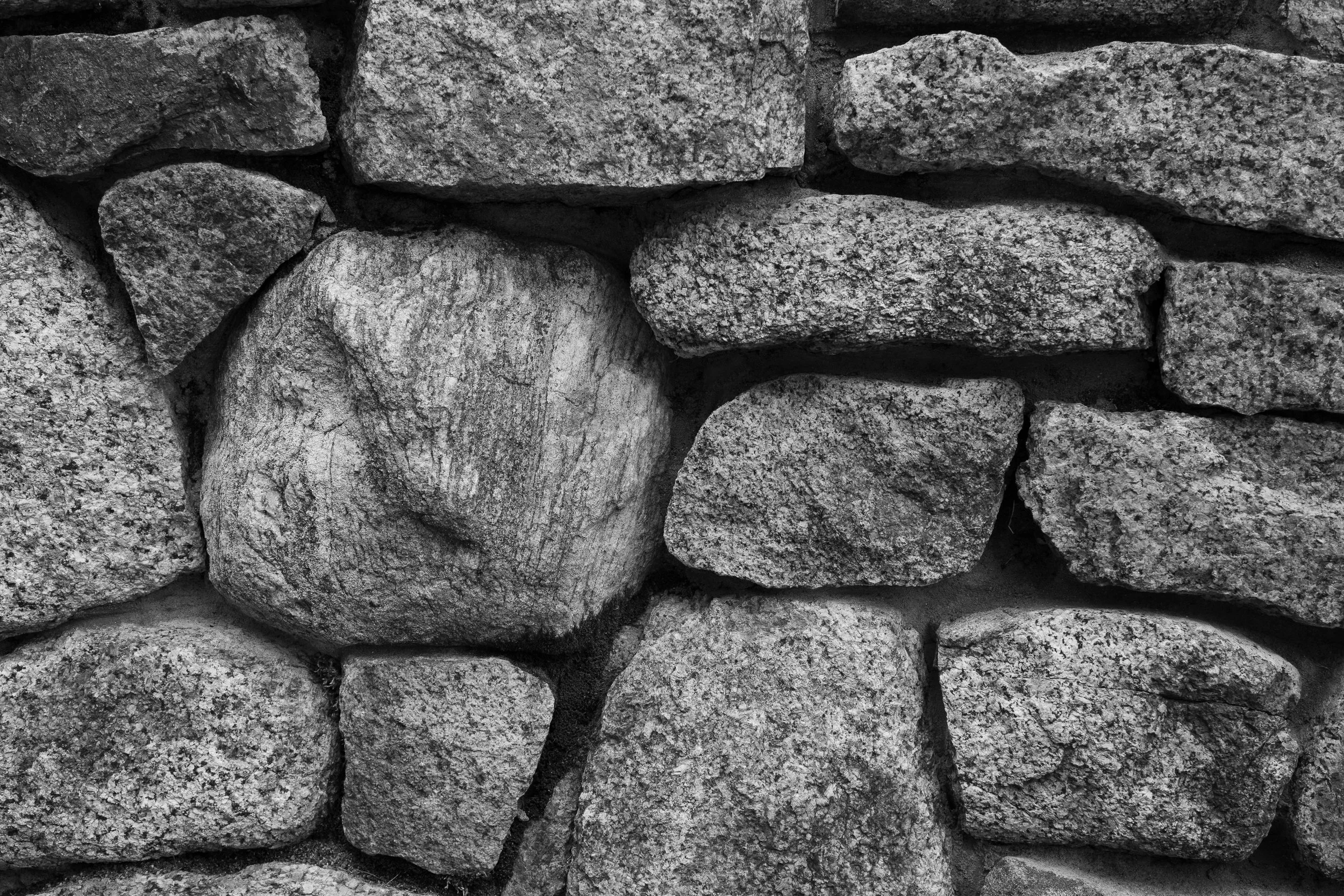 A close-up of a stone wall made of variously sized and shaped gray rocks stacked together.