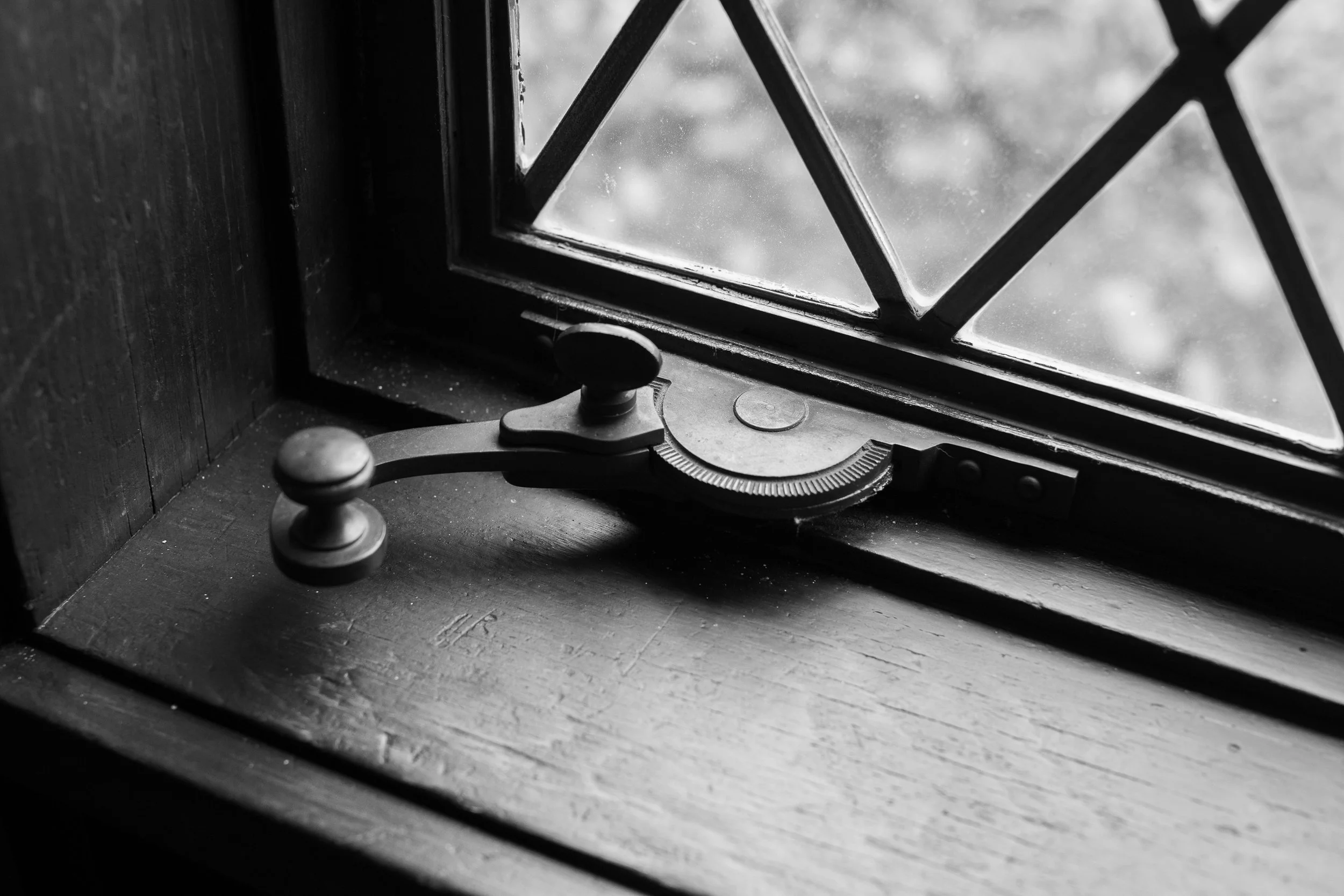 A black and white photo of a window with a metal armlock on the wooden windowsill.