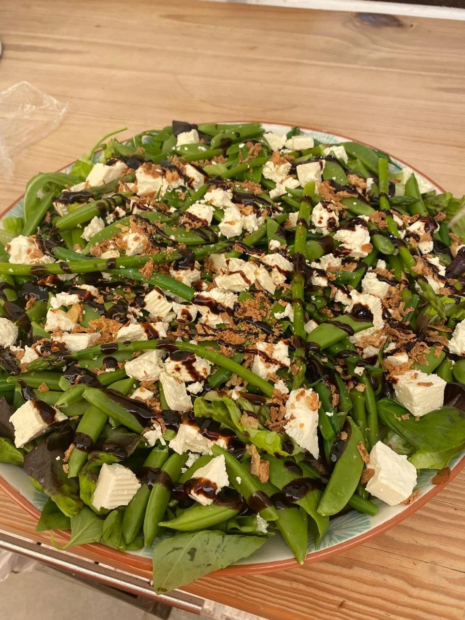 Mixed green salad with feta cheese, balsamic glaze, and crispy toppings on a plate.