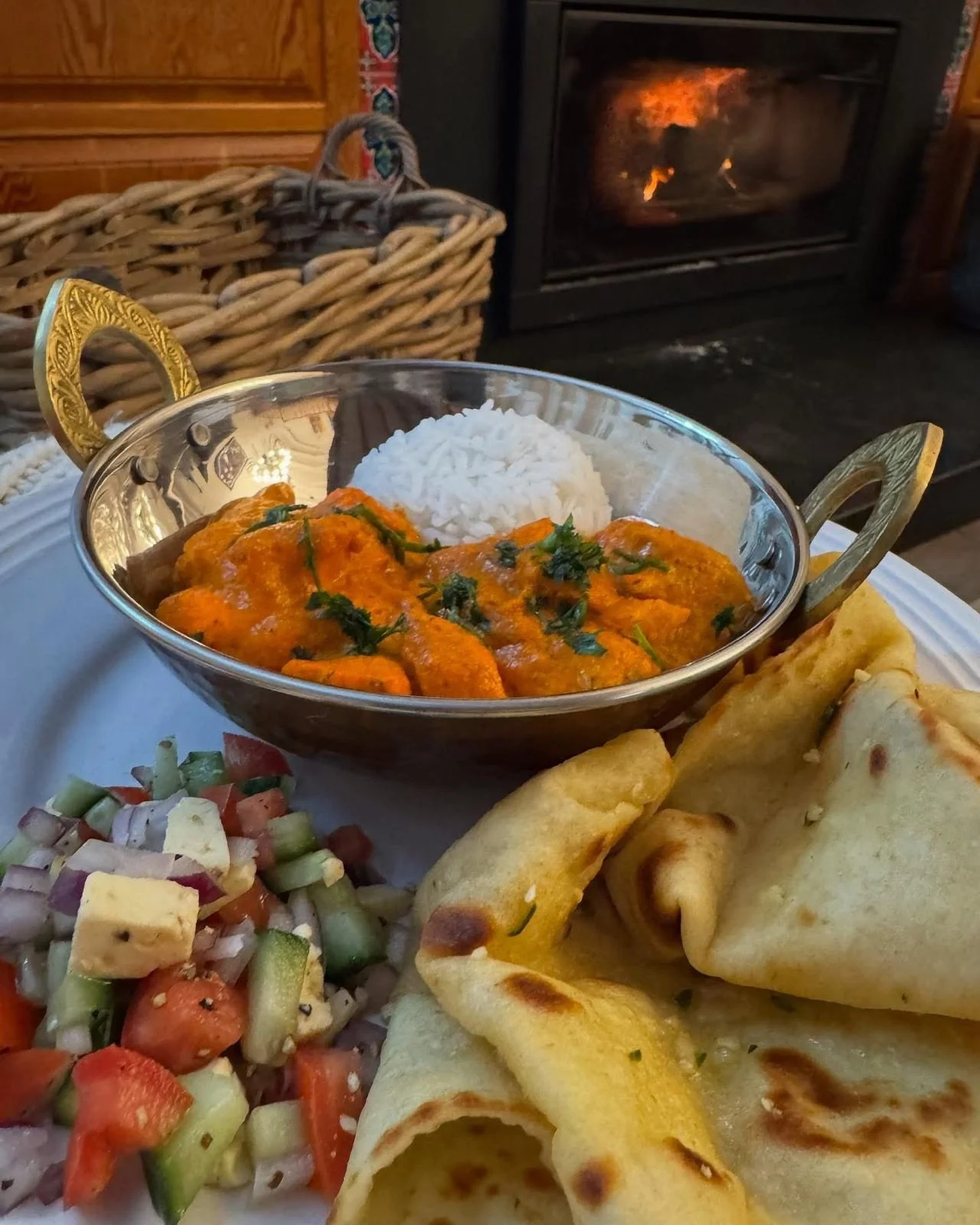 A plate of Indian food with rice, curry, naan bread, and a side salad, set in front of a fireplace.