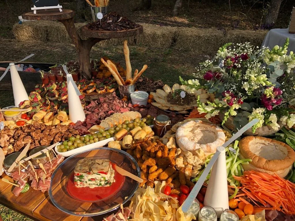 A table with various Arabic foods, salads, bread, and a large flower arrangement at an outdoor gathering.