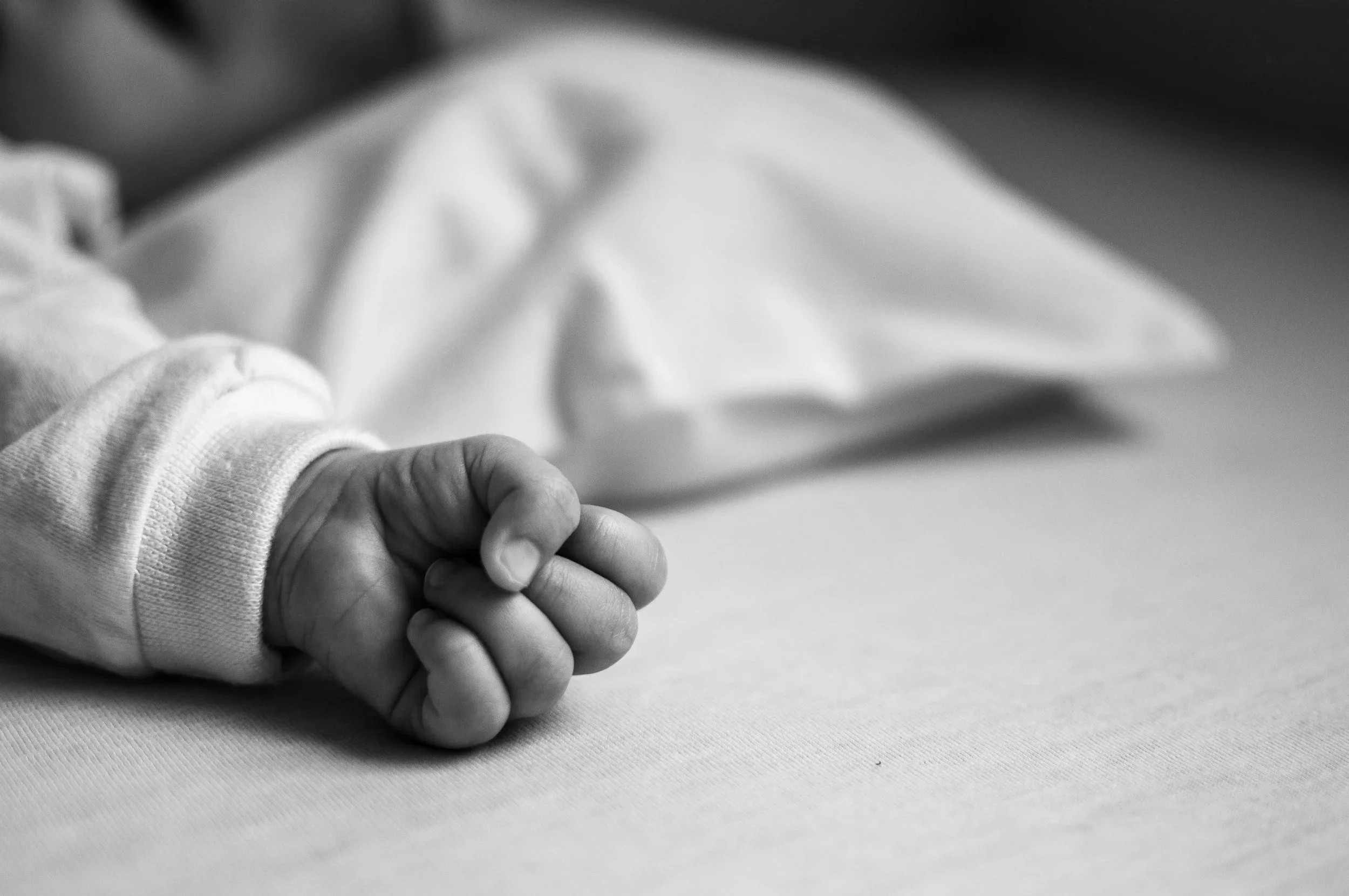 A close-up black and white photo of a small child's hand holding an adult's hand, resting on a flat surface.
