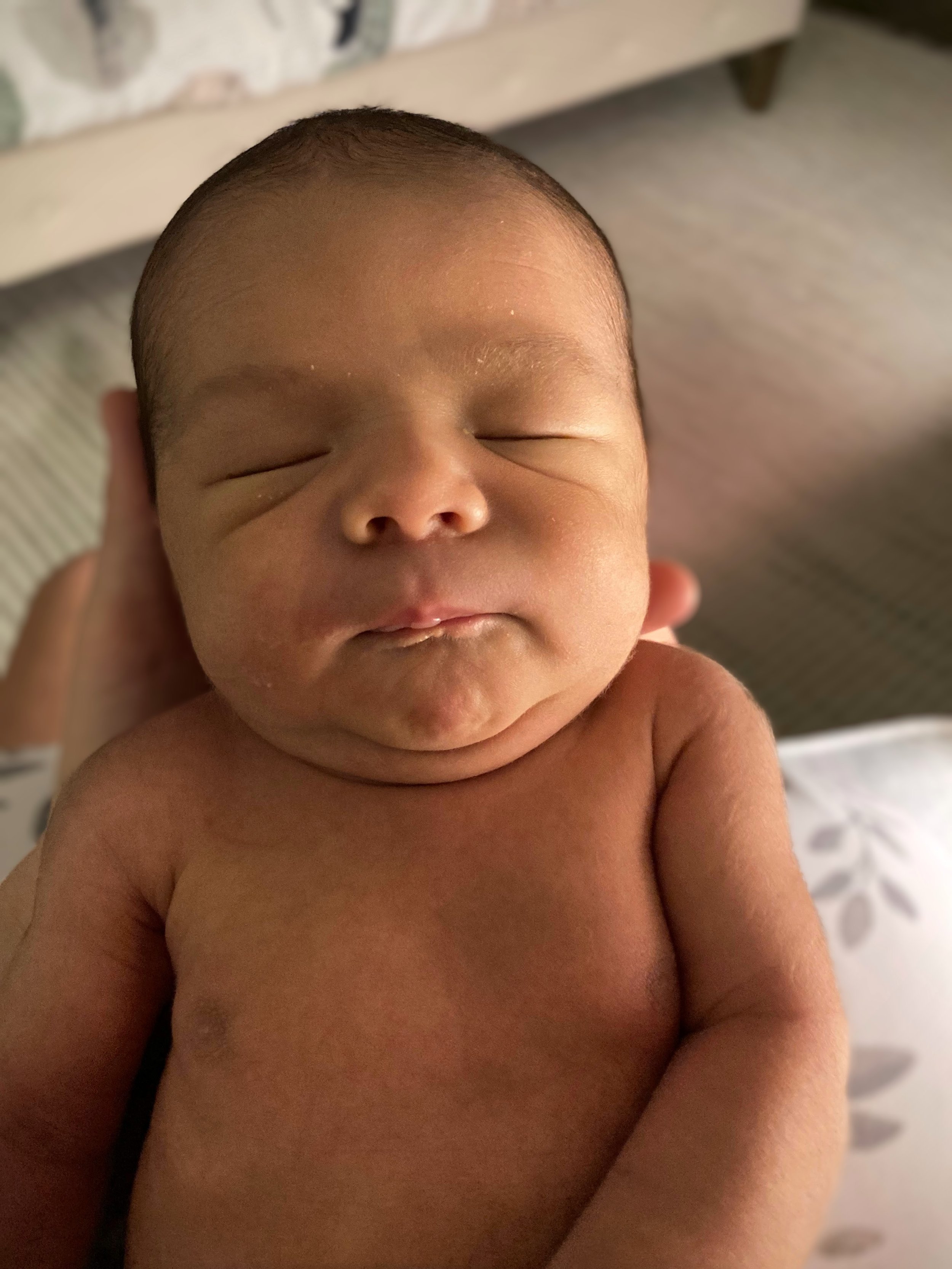 Close-up of a sleeping baby's face with eyes closed, lying on a bed.