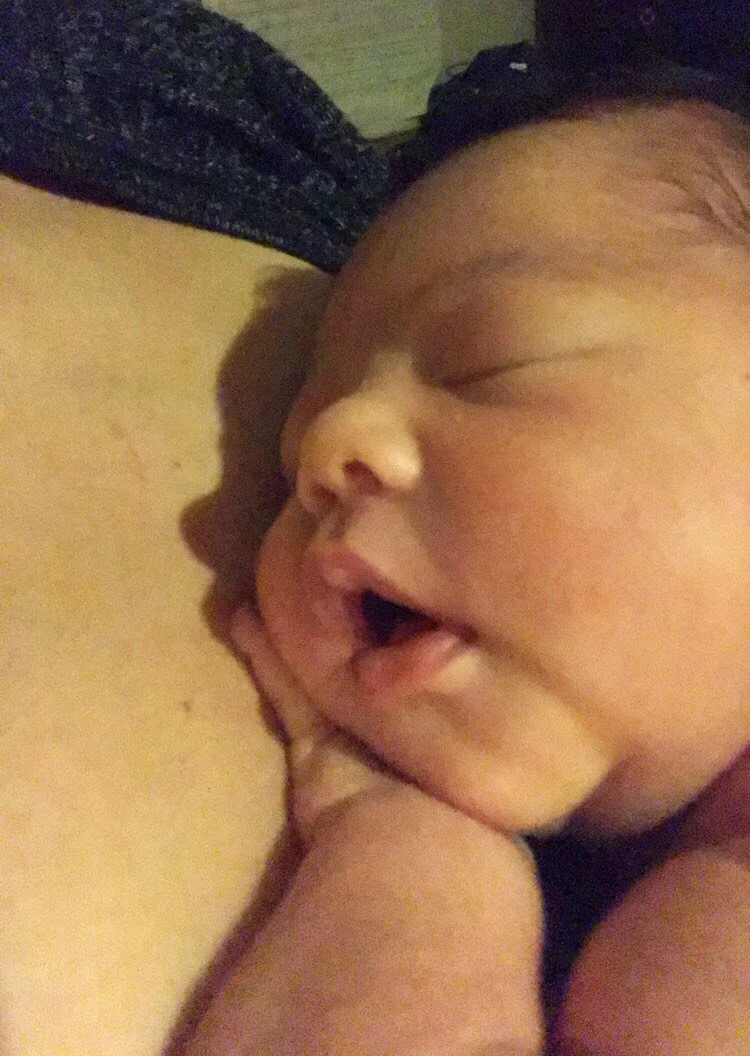 Close-up of a sleeping newborn baby resting on a person's chest.
