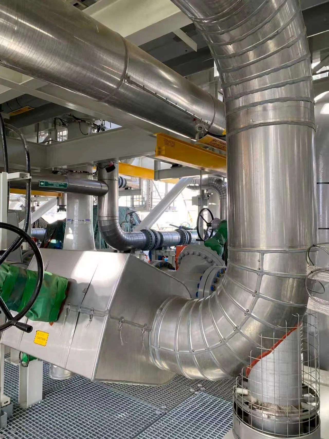Industrial piping system with large stainless steel pipes, valves, and ducts in a factory setting.