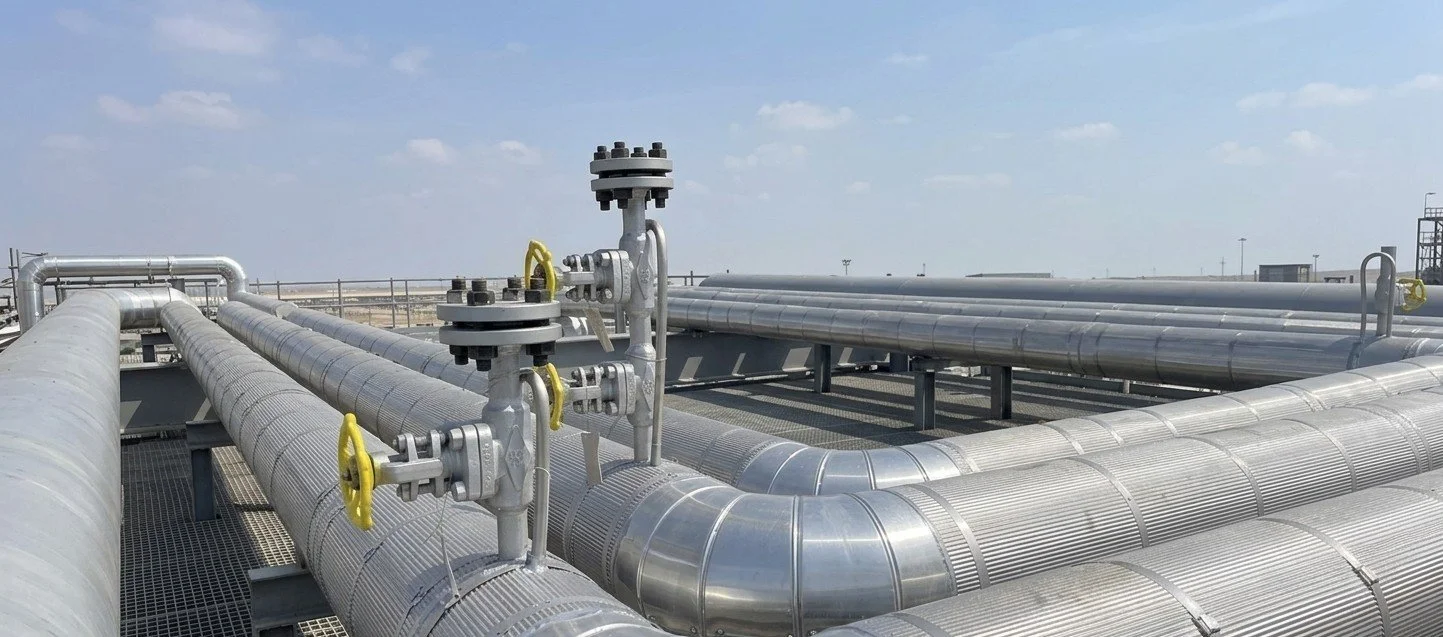 Industrial pipes and valves on a rooftop or platform under a blue sky.