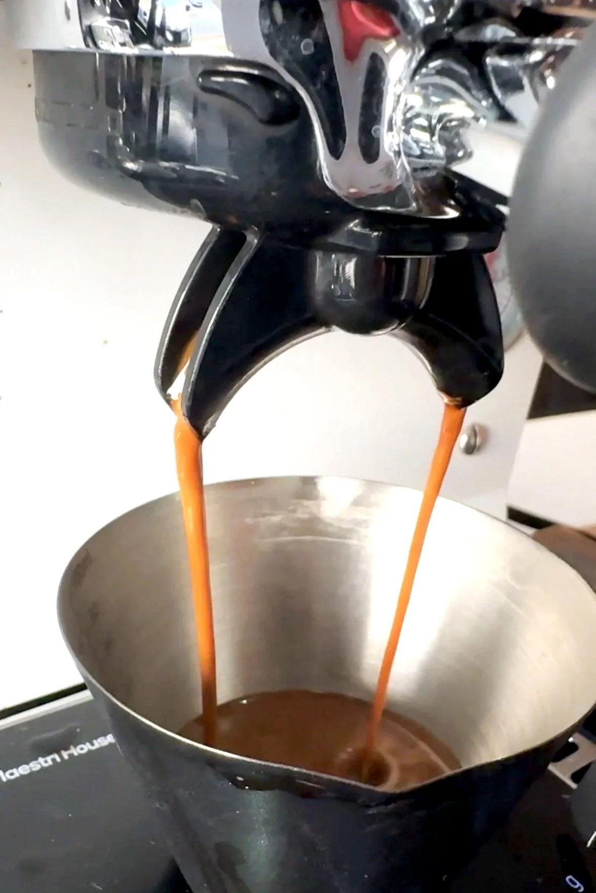 A double shot of espresso pouring into a metal shot cup, velvet and smooth
