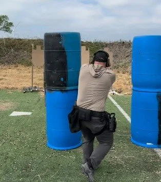 A person wearing a beige shirt, dark pants, and a cap practicing shooting at a shooting range with inflatable blue and black targets.