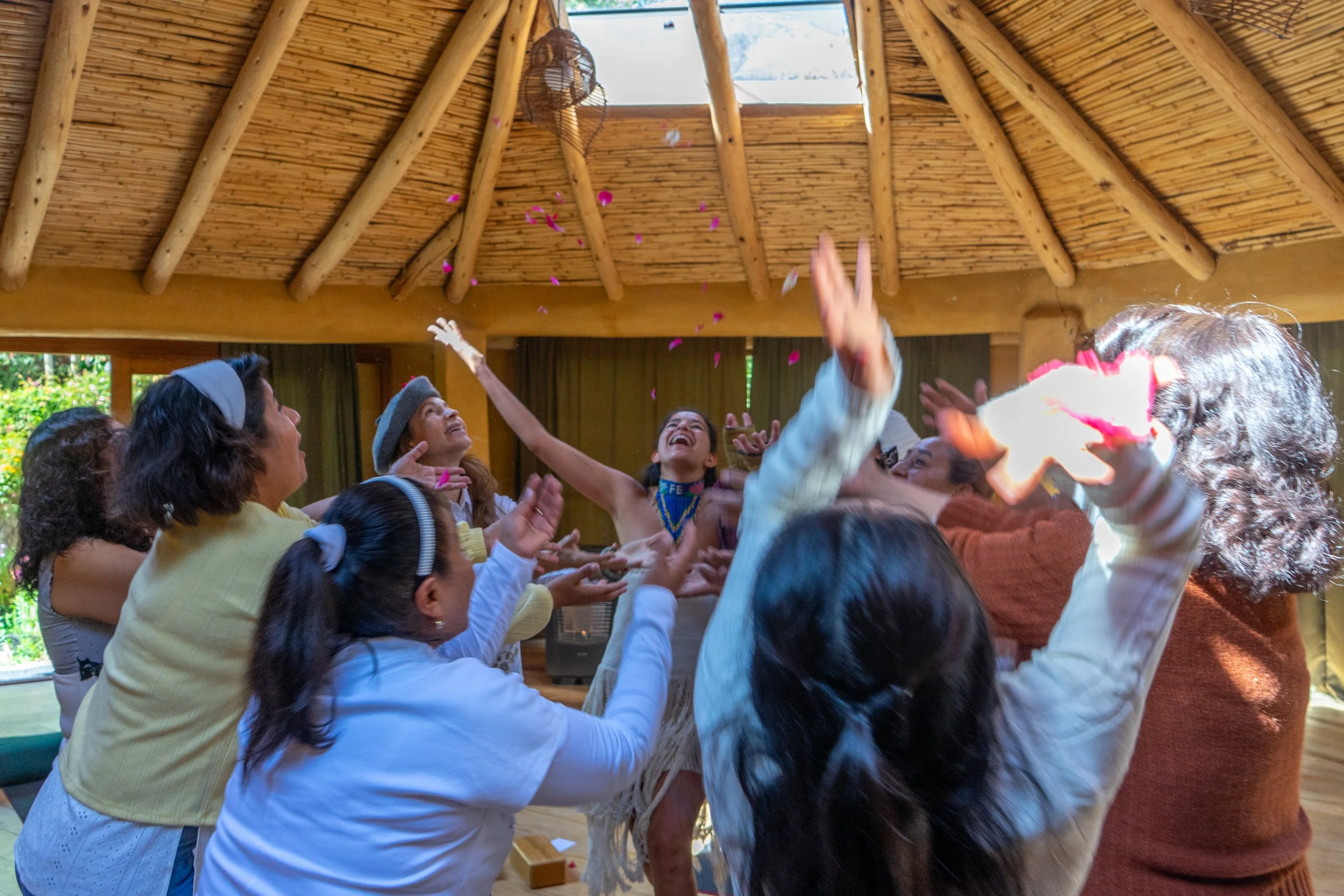 Group of people celebrating indoors, throwing pink flower petals into the air, with a wooden ceiling and a skylight above.