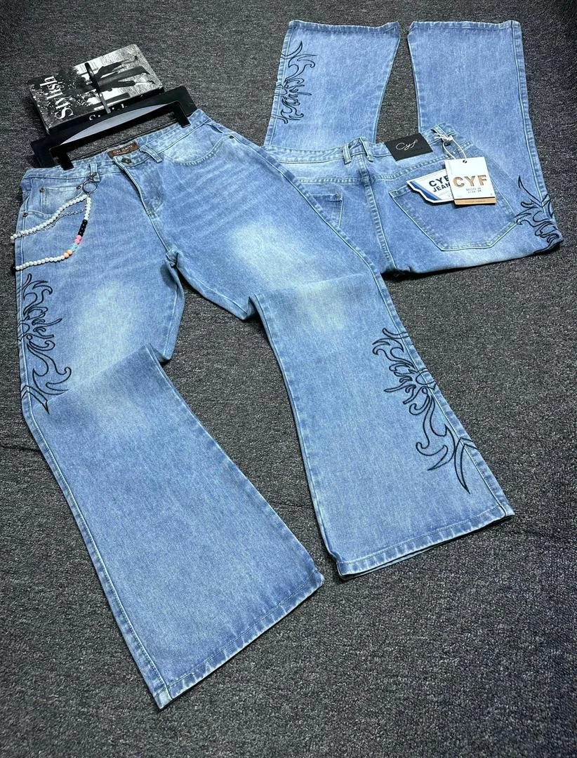 A pair of blue jeans with black floral embroidery on the legs, displayed on a dark surface.